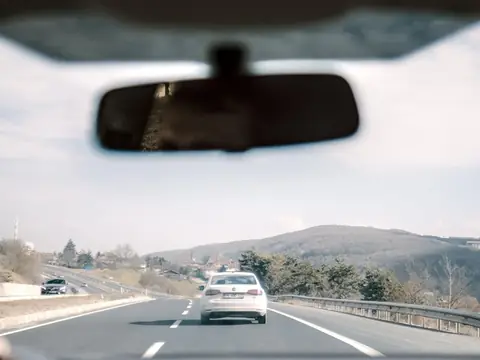 The rearview mirror at the top of a windshield, the road beyond